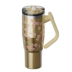 Gold insulated travel mug with pink cherry blossom pattern, clear lid, and beige handle, viewed from the side.