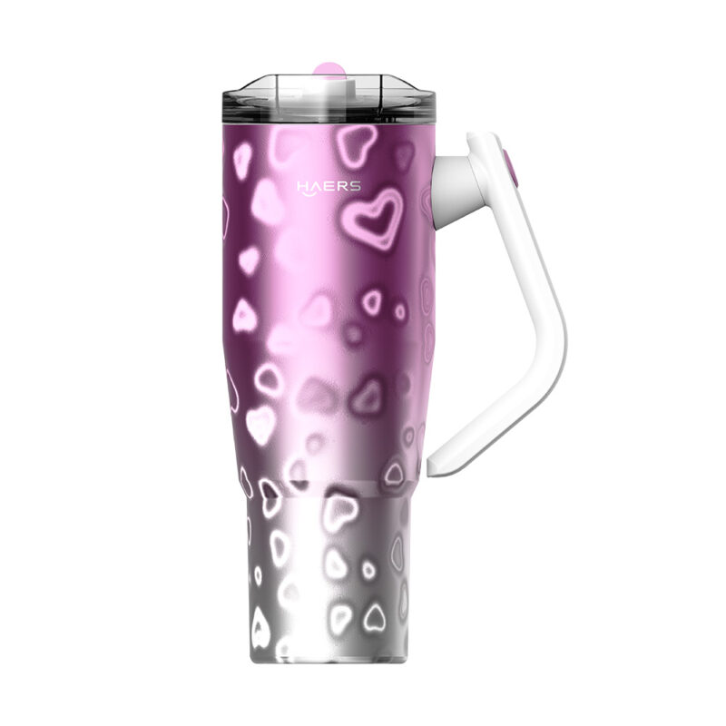 insulated travel mug with a pink-to-silver gradient and white heart patterns, clear lid, and white handle.