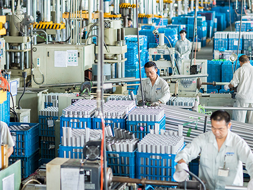factory floor with automated machinery, blue bins, and workers in white uniforms monitoring assembly lines in a large plant.