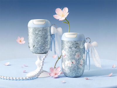 two blue floral insulated bottles with white lids, pearl chains, and pink petals on a pale blue surface.